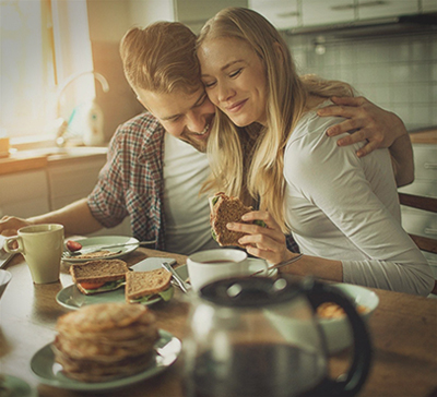 Мужчина и женщина с улыбками обнимаются за завтраком